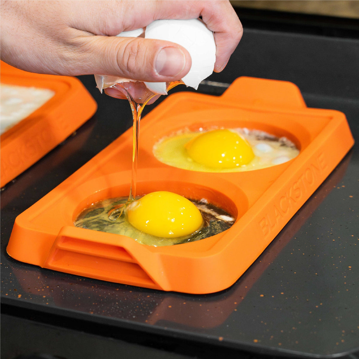 Blackstone 2 Section Silicone Egg Ring Trays, 3 Pack - Orange - cracking an egg into a tray