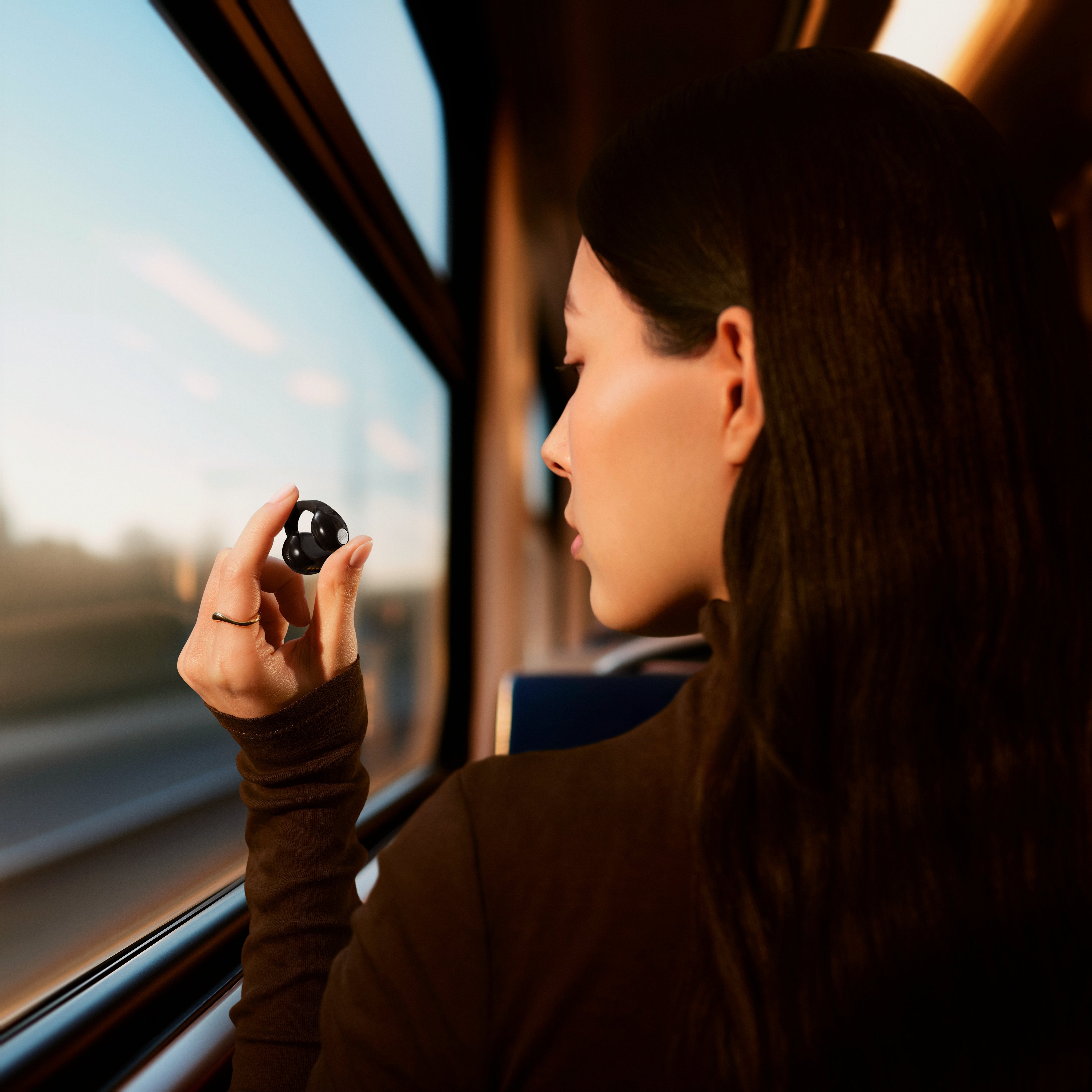 Sennheiser ACCENTUM Clip Open-Ear Earphones Black — lifestyle, held up on a train
